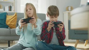 At Home Sitting on a Carpet: Cute Little Girl and Sweet Boy Playing in Competitive Video Game on two Smartphones, Holding them in Horizontal Landscape Mode. Close-up Portrait Camera Shot.