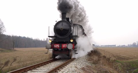 Old steam train running on the tracks in the countryside. Heritage historic steam locomotive with white smoke.