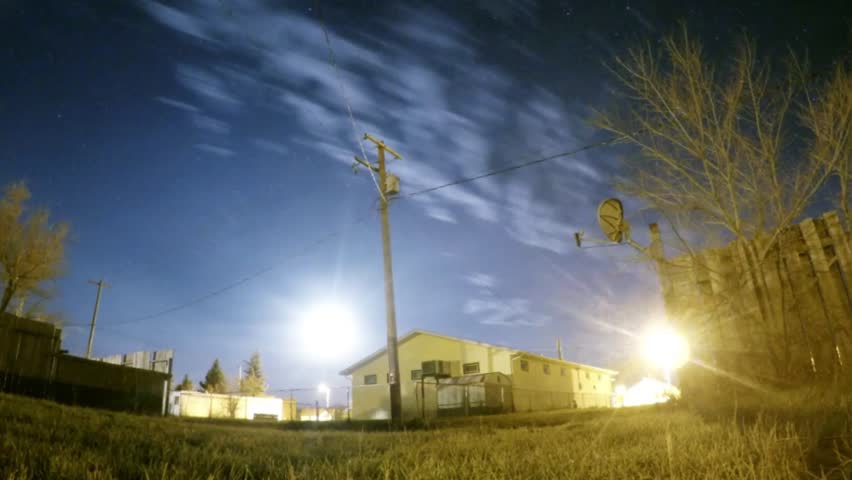 NIGHT NIGHT - Clouds and stars in the night sky above a building with street lights and bushes around.