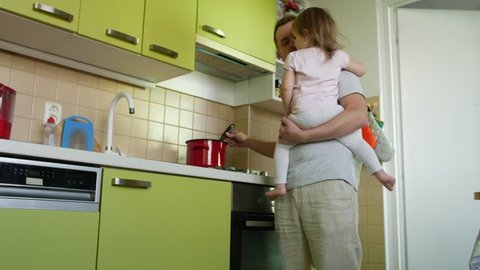 Father's day. Cooking father holding small daughter in arms lauds son for homework in kitchen. Dad making a meal, taking care of small girl and praising elder boy for lessons. Two children and parent