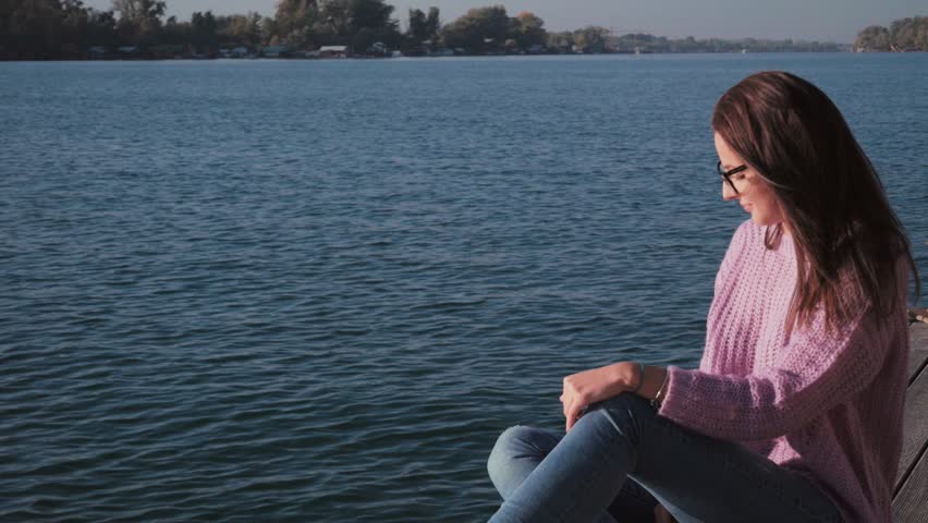 Girl sitting alone on the pier and looking at the river
