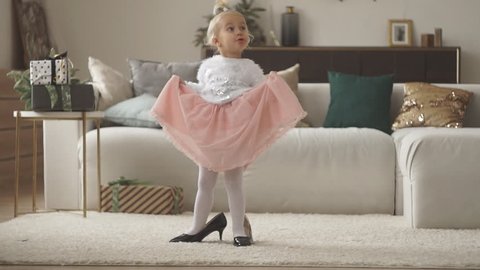 Pretty little girl in mom's shoes. Small fashionista trying on high heels at home