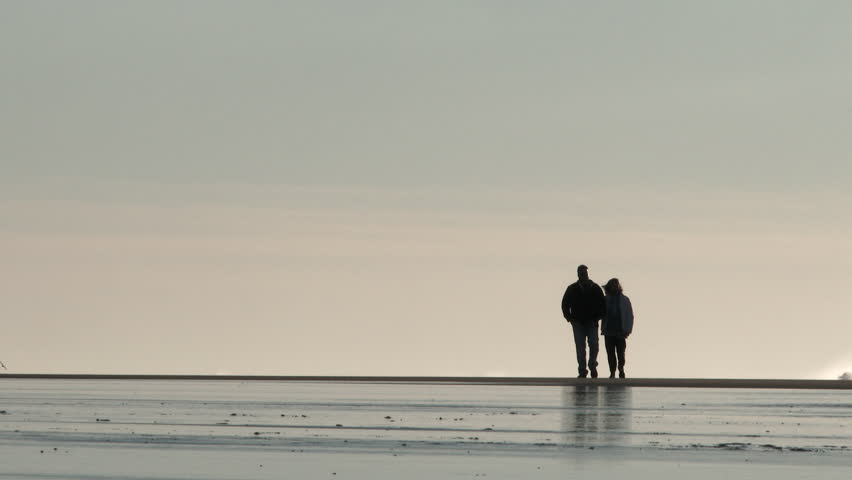 Unrecognizable silhouetted couple walk together on the Oregon Coast at low tide.