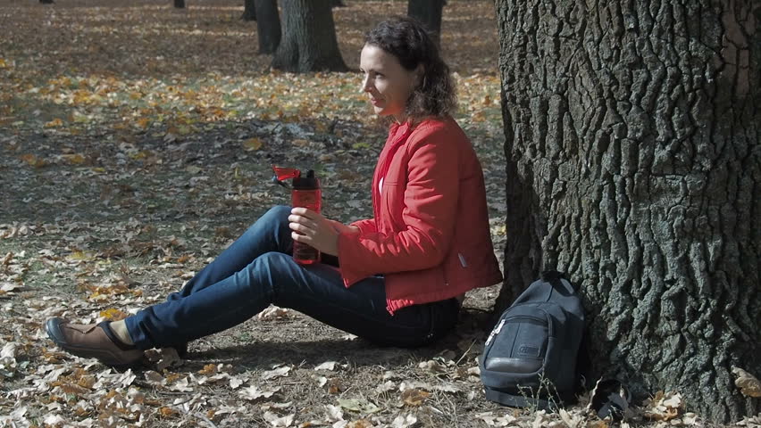 The girl drinks water park. Woman under the tree with a bottle of water.