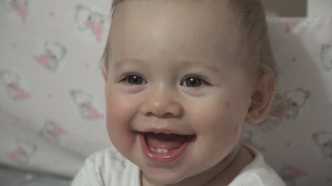 Close-up of a cute baby's face with beautiful big blue eyes smiling and laughing, showing first teeth