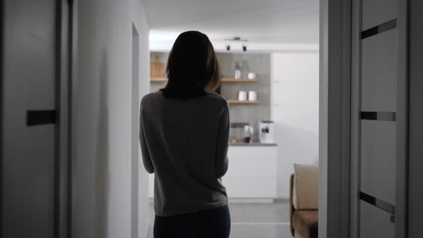 Young woman with short hair walking in kitchen, puts phone on the table and starts reading a book. | Shutterstock HD Video #1021189120