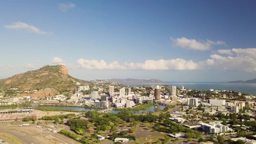 Drone moves right to left and slowly pans right while overlooking Townsville city and Castle Hill on a sunny morning.
