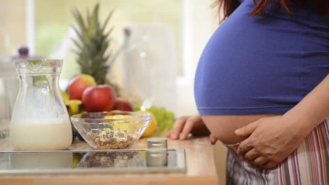 Pregnant woman pouring milk on cereals