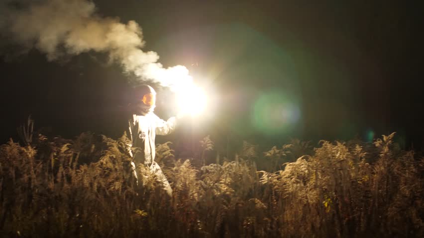 Along the grass, in the dark astronaut goes. In his hand a bright white light flashes