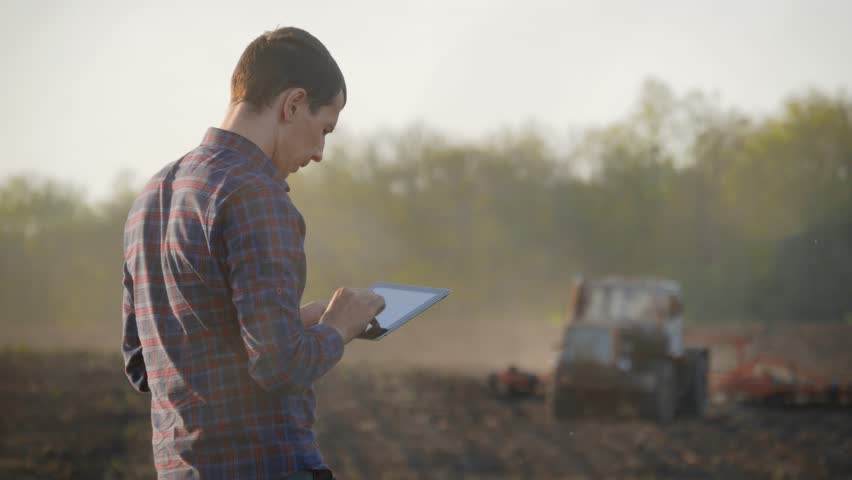 Farmer using digital tablet computer in cultivated field. Tractor in the background. Concept modern technology application in agricultural growing activity. Royalty-Free Stock Footage #1021204012