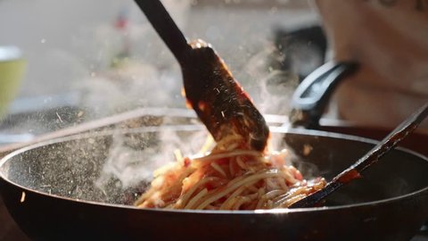 Cooking and stirring the spaghetti with red tomato sauce in the frying pan, close-up in slow motion