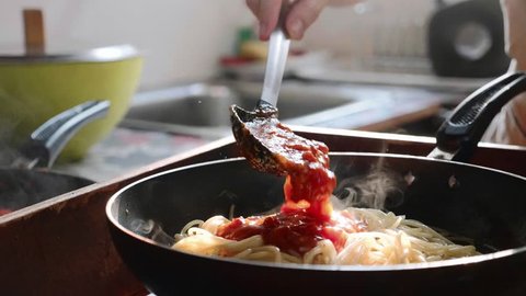 Cook adding tomato sauce on spaghetti in the frying pan, close-up in slow motion