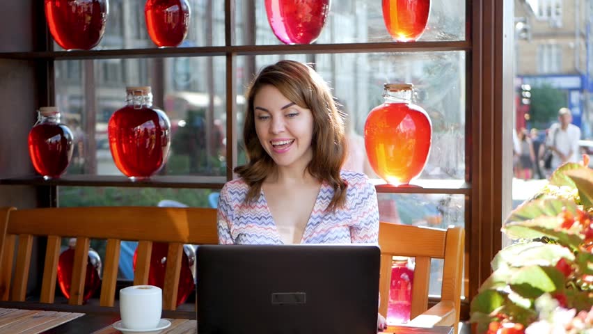 Smiling hipster girl talking and waving hand hello during online video call via laptop computer, sitting in coffee shop. Cheerful business woman having conference in internet via portable notebook | Shutterstock HD Video #1021211296