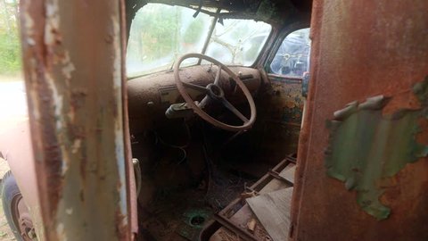 An old rusty truck abandoned at a deserted farm. Looking through the open driver's door as camera tilts up to reveal the weathered interior