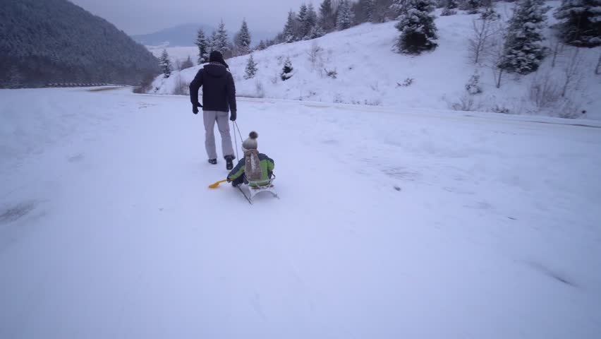 Young happy family having fun playing in a snowy forest. Father rolls his little son on a sled. An evening walk. Dad and his little son are happy together. Slow motion.
