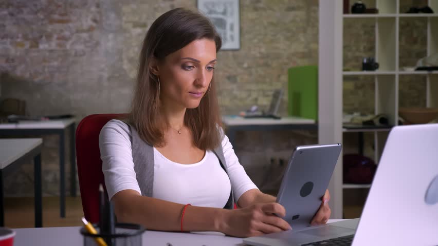 Attractiver female office worker browsing on the tablet smiling on the workplace indoors | Shutterstock HD Video #1021224208