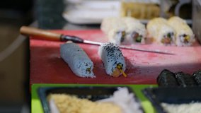 The waiter cuts some sushi with special knife on a wooden board. 4K video.