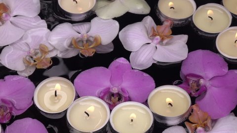 Slow motion of candle flames, floating among orchid flowers on waving dark water close up. Colorful beautiful natural floral background with lyric texture. High speed shooting without post processing.