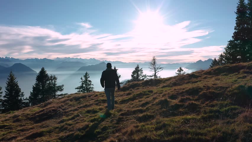 guy person walking slow motion on a mountain ridge looking into beautiful mountain scenery with fog covered lake sunny swiss alps rigi