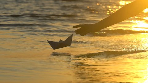 Kid child boy putting paper boat into water reflection of sun over beautiful sunset woman man child's hand launches paper ship on sea surface Ship sailing Dreams future childhood freedom hope concept