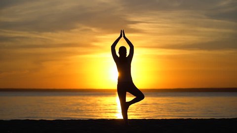 Silhouette sporty yoga woman doing tree yoga pose at sunset in nature outdoors. yoga poses, girl with open raised arms practicing yoga in sea water beach. Female working out training meditation, sun 