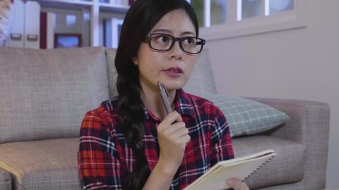 young female student wearing glasses writing memo on notebook thinking consider plan. college girl sitting at home at night study late prepare presentation. concentrated woman working hard midnight