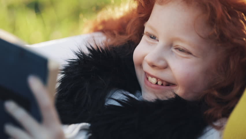 Mom and her little daughter sit in autumn part and read a book. They talk nicely. Happy family in the autumn forest. Slow motion