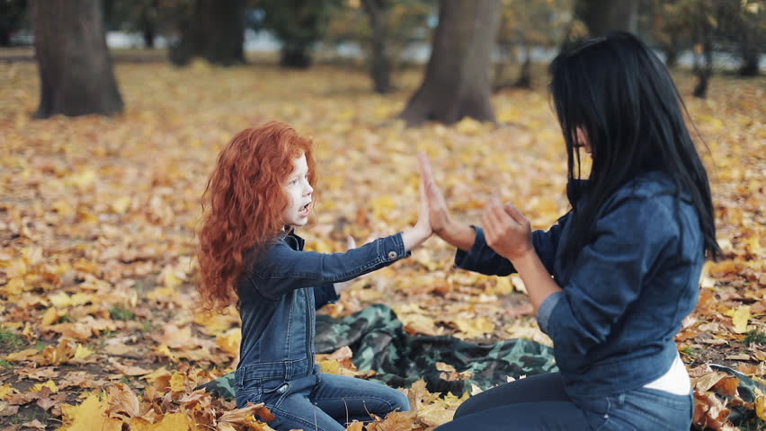 Little redhead girl with her mommy spend time in autumn park. They play and clap hands