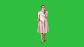 Smiling woman in pink dress doing making video call and walking on a Green Screen, Chroma Key.