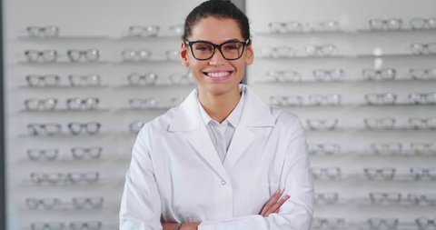 Portrait of a beautiful  woman oculist in white robe smiling satisfied with her work in an optical center. Concept of eyecare, glasses, optic, lens