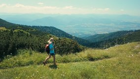 Woman tourist walking on the top of mountain in summer sunny day under sun light. Beautiful mountains landscape view. Aerial View Drone 4K Video.