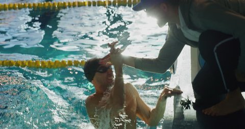 Professional swimmer is encouraged by his coach for new record achievement. Shot with RED Camera in 8K. Concept of sport, swimming pool, competition, fitness.