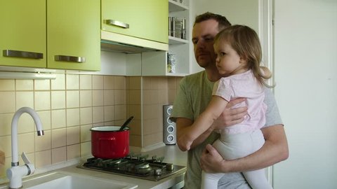 Father's day. Cooking father with small daughter in hands praising son for writing in kitchen, family smiling. Super dad taking care of toddler girl and making a meal lauds boy for correct work sheet
