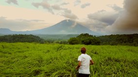 Drone following boy running through tall grass to reveal Mt. Agung Volcano in Bali, Indonesia
