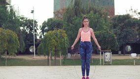 Slowmotion video of Fit beautiful woman with jumping rope in a park. Fitness female doing skipping workout outdoors on a sunny day.