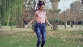 Slowmotion video of Fit beautiful woman with jumping rope in a park. Fitness female doing skipping workout outdoors on a sunny day.