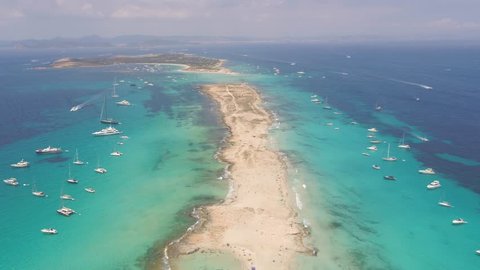 Aerial view of the white sandy beach of Formentera, moving in a forward direction at high speed. A perfect establishing shot of the entire beach.