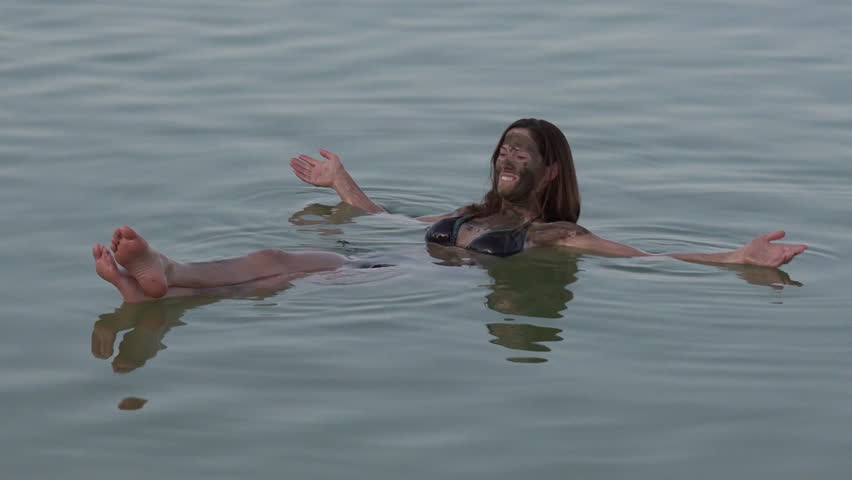 Young woman with natural mineral mud on her body floating on the Dead Sea, Israel