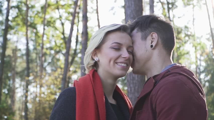 Young smiling couple in love kissing on a background of pine trees and sunset light. Multi ethnic couple in love.