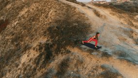 Woman is doing yoga High Lunch Pose on the top of mountain at sunset. Aerial beautiful footage.