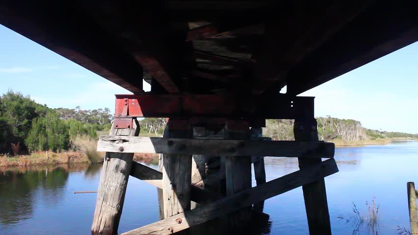 A shot underneath an old wooden railway bridge in Victoria Australia with the reflection of the water from the river shining on the bridge.