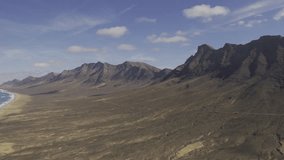 Aerial (10 bit UNGRADED ) of a long beach and a mountain range. Island of Fuerteventura neaf Cofete. UHD Video Footage