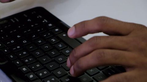 Close up of brown Indian hands typing on a qwerty keyboard of a touch screen tablet 
