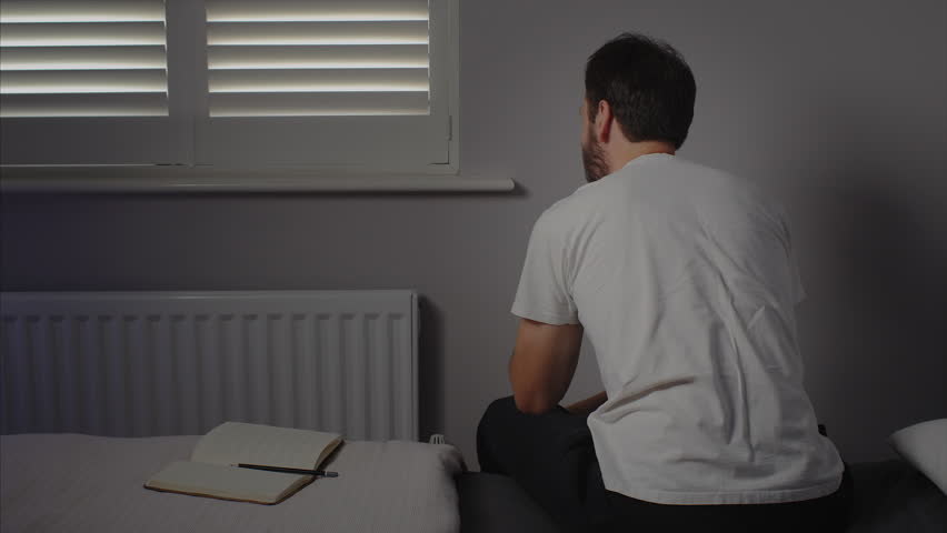 WIDE SHOT of a married man, in a minimalistic bedroom, suffering from depression and having a panic attack.
