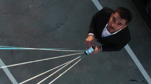 Big City Businessman Uses Smartphone, Stands on Skyscraper Roof: Visualization of Information Flows and Lines Flying from Mobile Phone into Global Network. Top Down Aerial Elevating Drone Shot.