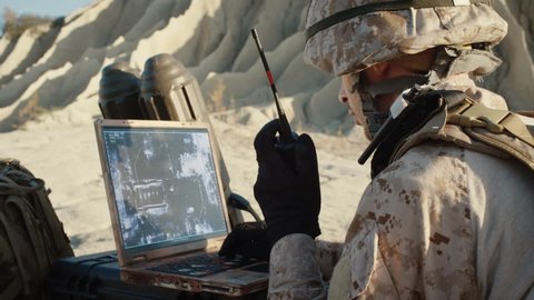 Military Operation in the Desert, Using Satellite or Drone Technology: Soldier with Laptop Monitors Movement of Armed Terrorist Vehicle, Uses Radio Communication to Call an Air Strike.