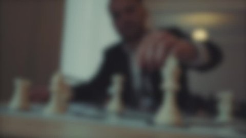Blurred background, a man makes a move in chess, plays against himself