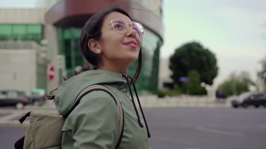 Pretty girl standing in city center looking around smiling. Young attractive female backpacker seeing sights around her in new city on background of traffic. Slow motion. Travel concept. Royalty-Free Stock Footage #1021309585