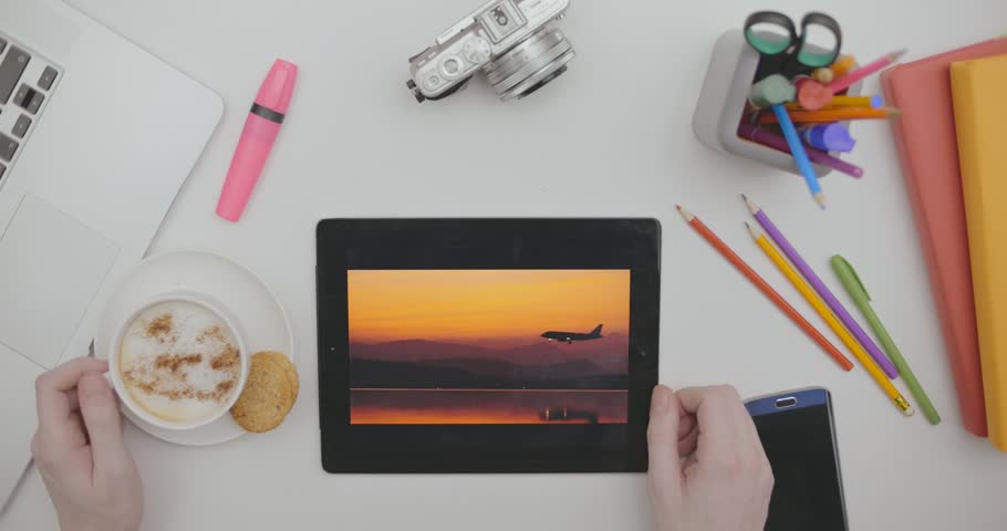 Male hand scrolling vacation photos on dislpay tablet. Working and thinking about vacation, remembering the rest and looking at photos