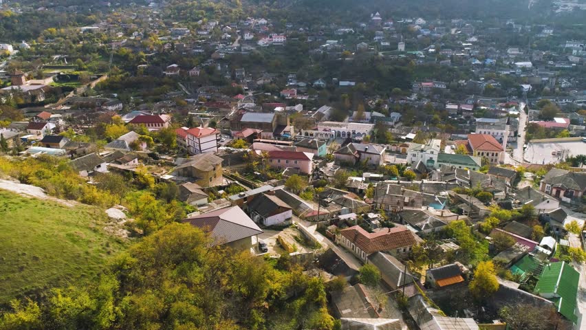 Top view of city located in valley with hills. Shot. Life in city, located between the wooded hills like resort. Summer, sun, greenery and town with forest and hills